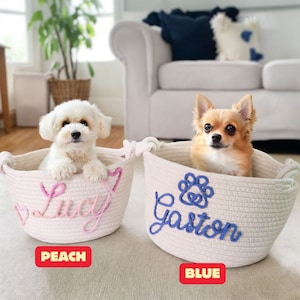 May include: Two white rope dog beds with personalized names. The bed on the left is pink and says "Lucy" and the bed on the right is blue and says "Gaston".