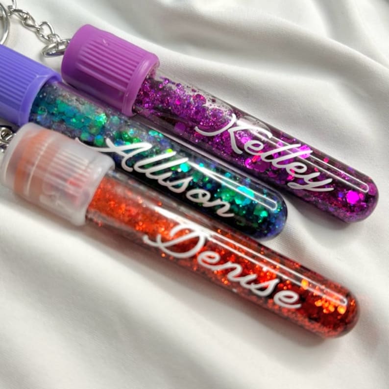 Pu&ograve; includere: Tre tubi di plastica trasparente riempiti di glitter colorati e sormontati da tappi viola. Ogni tubo ha un nome scritto su di esso: Kelley, Allison e Denise.