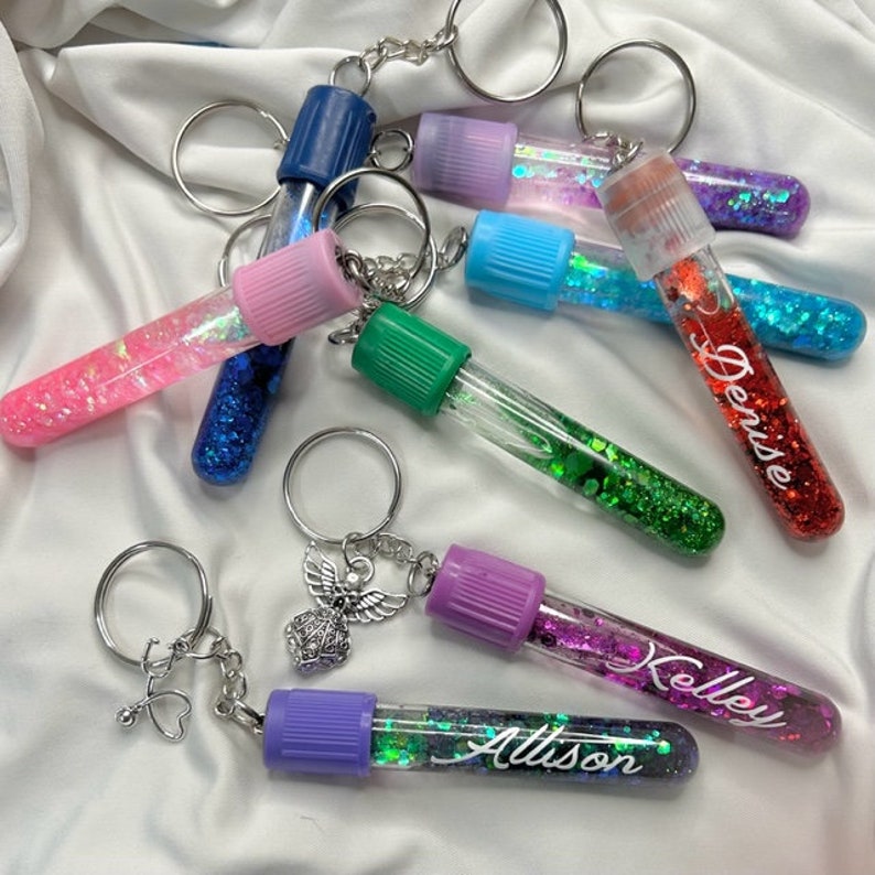 Pu&ograve; includere: Sette tubi portachiavi colorati pieni di glitter con anelli portachiavi argentati. I tubi sono etichettati con i nomi "Allison", "Kelley", "Derese" e altri.