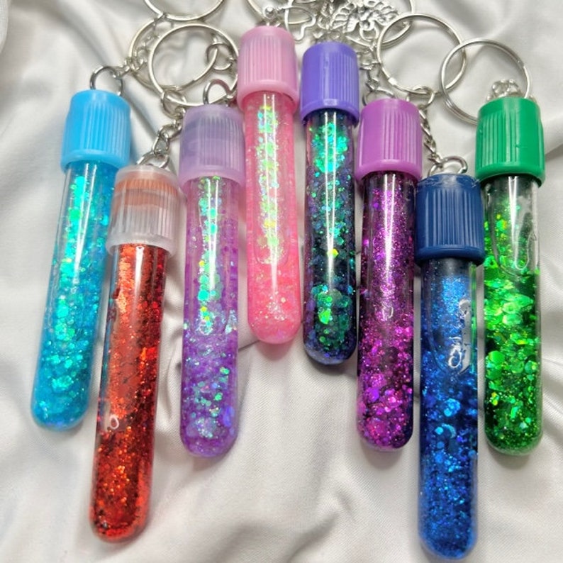 Pu&ograve; includere: Un set di dieci tubi portachiavi pieni di glitter colorati. I tubi sono in vetro trasparente con una variet&agrave; di colori, tra cui blu, verde, rosso, viola e rosa. Ogni tubo ha un portachiavi in metallo argentato.
