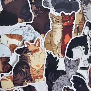 Op de afbeelding: Een verzameling kattenstickers in verschillende kleuren en patronen. De stickers tonen cartoon-achtige illustraties van katten in verschillende poses, sommige knuffelend of interactie. De katten hebben diverse vachtkleuren, waaronder bruin, zwart, grijs en oranje.
