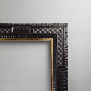 Könnte beinhalten: Ein schwarzer Holzrahmen mit goldener Innenkante. Der Rahmen hat ein dekoratives, strukturiertes Design.