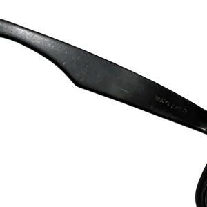 K&ouml;nnte beinhalten: Schwarzer Kunststoff-Brillenb&uuml;gel mit dem Aufdruck "WAYFARER?". Der B&uuml;gel ist gebogen und hat eine matte Oberfl&auml;che.