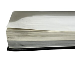 May include: A thick, bound book with a black cover. The pages are a mix of white, off-white, and gray, creating a layered effect. The book is open, revealing the stacked pages.