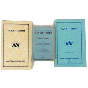 May include: Three book covers for the Constitution of the United Transportation Union. The covers are all blue, green, and yellow. The text on the covers reads "Constitution" and "United Transportation Union".
