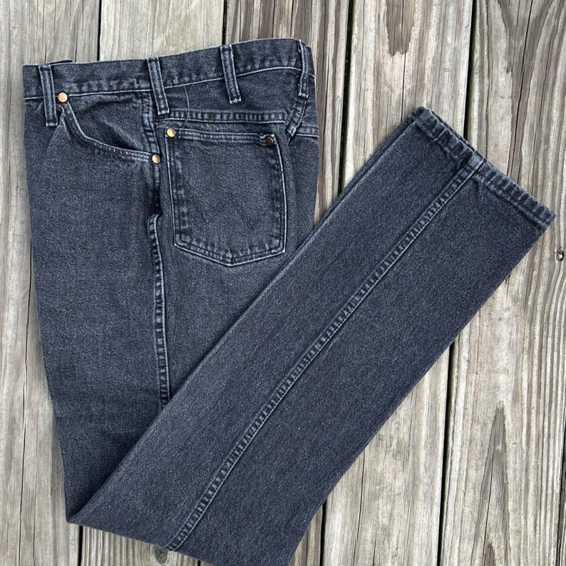 May include: Dark gray denim jeans with a classic five-pocket design. The jeans have a straight leg cut and feature copper rivets and a button closure. The fabric appears to be pre-washed for a worn-in look.