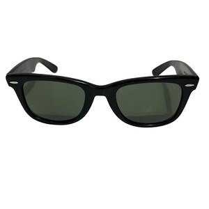 K&ouml;nnte beinhalten: Schwarze Sonnenbrille mit klassischem, rechteckigem Rahmen und dunkelgr&uuml;nen Gl&auml;sern. Die Sonnenbrille hat eine gl&auml;nzende Oberfl&auml;che und einen dezenten, silbernen Akzent auf jeder Seite des Rahmens. Die B&uuml;gel sind leicht gebogen.