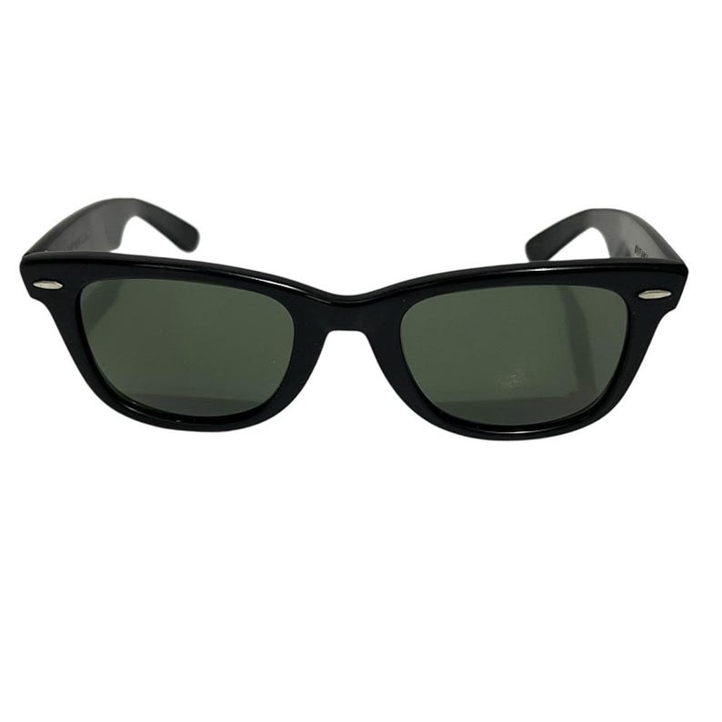 K&ouml;nnte beinhalten: Schwarze Sonnenbrille mit klassischem, rechteckigem Rahmen und dunkelgr&uuml;nen Gl&auml;sern. Die Sonnenbrille hat eine gl&auml;nzende Oberfl&auml;che und einen dezenten, silbernen Akzent auf jeder Seite des Rahmens. Die B&uuml;gel sind leicht gebogen.