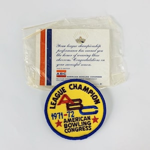 Puede incluir: Un parche bordado amarillo y azul con el texto "League Champion 1971-72 American Bowling Congress". El parche presenta un logotipo "ABC" estilizado en rojo, marrón y azul.