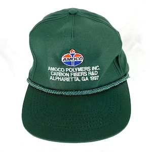 Puede incluir: Gorra de béisbol verde oscuro con visera curva y detalle de cuerda. La gorra presenta el logotipo "AMOCO" en rojo, blanco y azul, junto con el texto "AMOCO POLYMERS INC. CARBON FIBERS R&D ALPHARETTA, GA 1997".