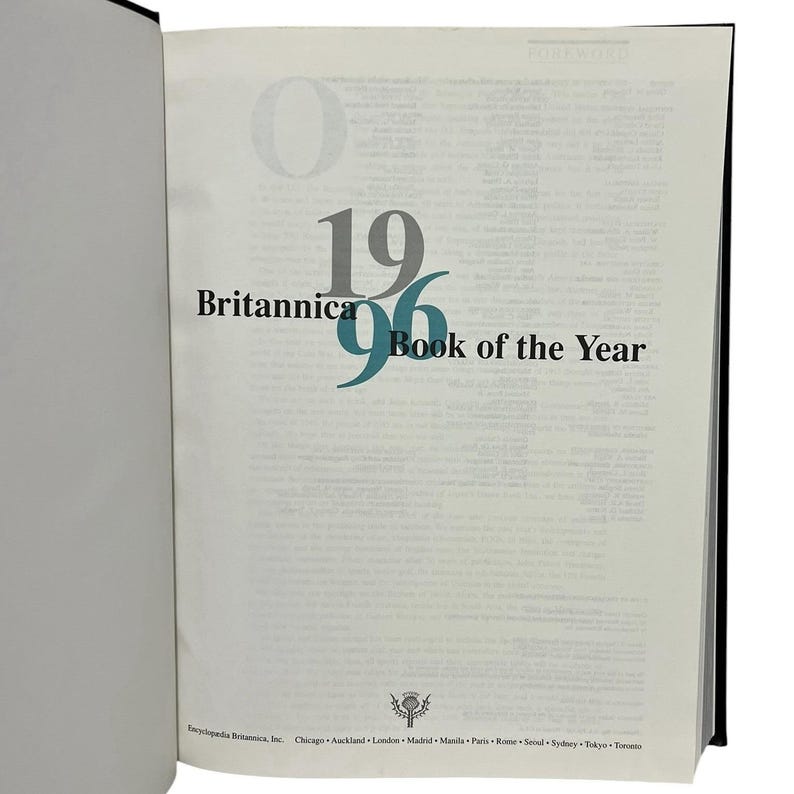 May include: An open book showing the title "Britannica 1996 Book of the Year". The text is in black and teal. The book's spine is black, and the pages are off-white.
