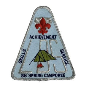 Może przedstawiać: Jasnoniebieska trójkątna naszywka ze srebrnym obramowaniem. Naszywka przedstawia czerwony motyw fleur-de-lis, słowo "ACHIEVEMENT" oraz litery "LBS" z zieloną grafiką namiotu. Słowa "SKILLS" i "SERVICE" znajdują się po bokach, a "88 SPRING CAMPOREE" na dole.