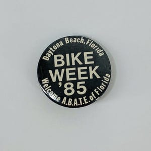 May include: Black and white button with the text "Daytona Beach, Florida Bike Week '85 Welcome A.B.A.T.E. of Florida"