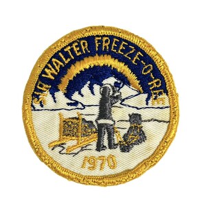 May include: A round, yellow embroidered patch with a white background. The patch features a blue sky with a yellow sun, a person standing in the snow, and the text "Sir Walter Freeze-O-Ree 1970".