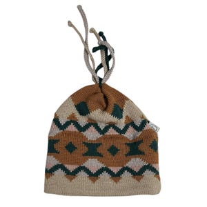 Może przedstawiać: Dzianinowa czapka typu beanie z geometrycznym wzorem w kolorze brązowym, zielonym, różowym i beżowym. Czapka posiada ściągacz ze sznurkami w kolorze beżowym i zielonym. Mała metka jest przymocowana z boku.