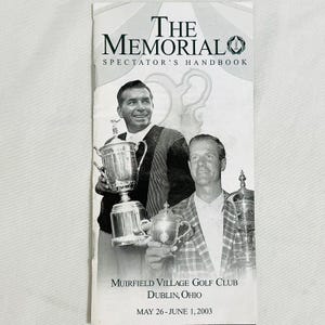 May include: A black and white photo of two men holding trophies. The text "THE MEMORIAL SPECTATOR'S HANDBOOK" is at the top of the image. The text "MUIRFIELD VILLAGE GOLF CLUB DUBLIN, OHIO MAY 26-JUNE 1, 2003" is at the bottom of the image.