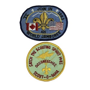 May include: Two embroidered patches, one blue with the text "JOIN IN 1983 WORLD JAMBOREE" and a fleur-de-lis, and one green with the text "CATCH THE SCOUTING SPIRIT 1983 OCCONEECHEE SCOUT-O-RAMA" and a fleur-de-lis.
