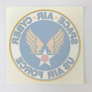 May include: A blue and white circle sticker with the text "US AIR FORCE SPACE CYBER" around the outside. The center of the circle features a white star with a pink center and two light pink wings.