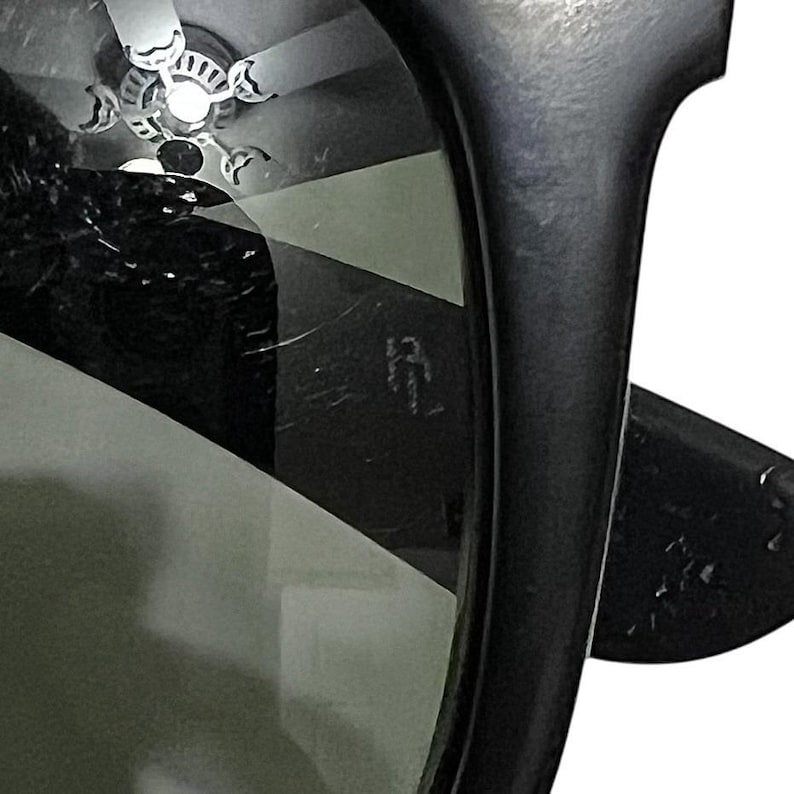 K&ouml;nnte beinhalten: Nahaufnahme einer schwarzen Sonnenbrille mit dunklen Gl&auml;sern. Der Rahmen ist dick und scheint aus Kunststoff zu sein. Die Linse reflektiert einen Deckenventilator und andere Objekte.