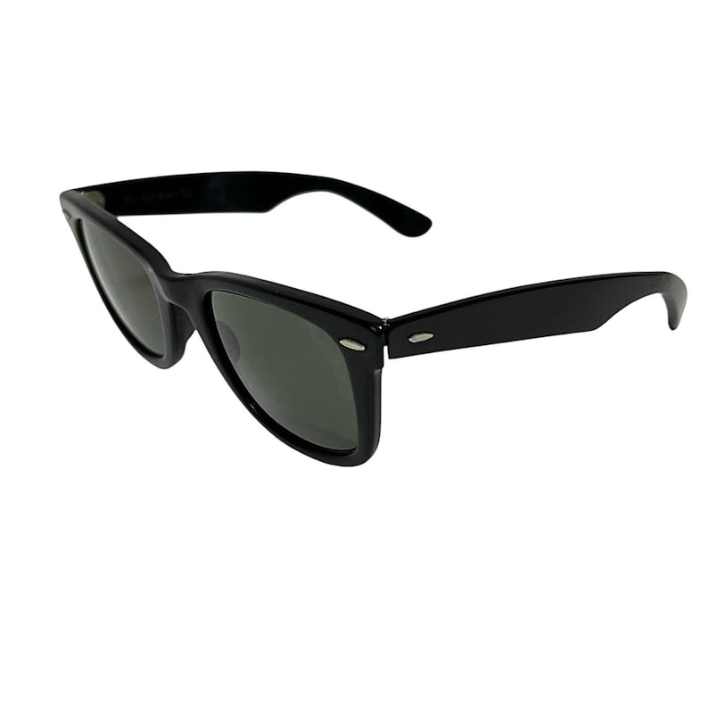 K&ouml;nnte beinhalten: Schwarze Sonnenbrille mit klassischem Design. Die Rahmen sind gl&auml;nzend schwarz und die Gl&auml;ser sind dunkelgrau. Die Sonnenbrille hat eine rechteckige Form mit einer leichten Aufw&auml;rtsneigung an den &auml;u&szlig;eren Ecken.