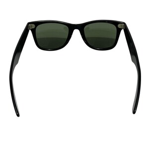 K&ouml;nnte beinhalten: Schwarze Sonnenbrille mit dunkelgr&uuml;nen Gl&auml;sern. Die Sonnenbrille hat ein klassisches rechteckiges Rahmendesign. Die B&uuml;gel der Sonnenbrille sind ausgeklappt und zeigen die Scharniere und die Form des Rahmens. Die Gl&auml;ser sind leicht reflektierend.