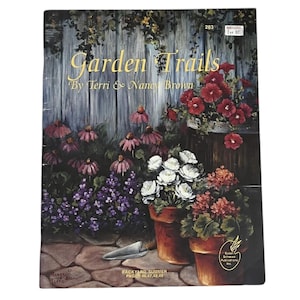 May include: A book cover titled "Garden Trails" by Terri & Nancy Brown. The cover features a painting of a garden scene with flowers in pots, a wooden fence, and the text "Backyard Summer Pages 46,47,48,49".