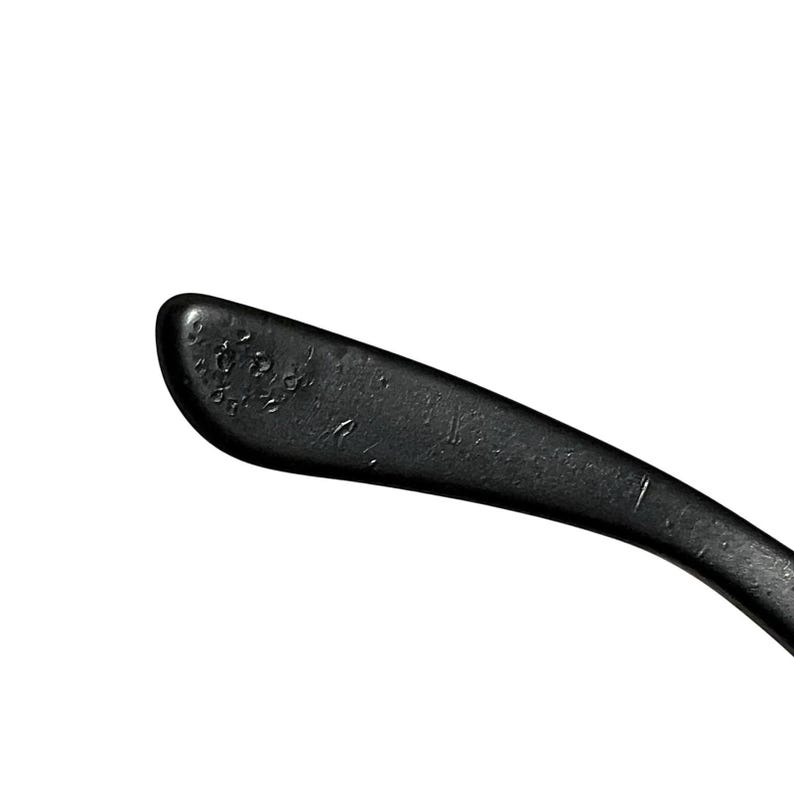 K&ouml;nnte beinhalten: Nahaufnahme eines schwarzen Brillenb&uuml;gels. Der B&uuml;gel ist gebogen und hat eine matte Oberfl&auml;che. Das Ende des B&uuml;gels hat eine abgerundete Form mit kleinen, strukturierten Details. Der Hintergrund ist schlicht wei&szlig;.