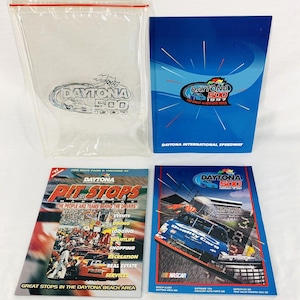 Puede incluir: Una colección de cuatro artículos relacionados con la carrera Daytona 500. Una bolsa de plástico transparente con el logotipo de Daytona 500, un folleto azul con el logotipo de Daytona 500 y el texto "Daytona International Speedway", una revista titulada "Pit Stops" con el logotipo de Daytona 500 y el texto "The People and Teams Behind the Drivers", y un folleto azul con el logotipo de Daytona 500 y una imagen de un coche de carreras.