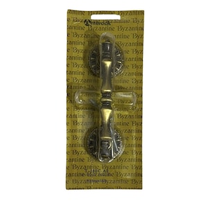 May include: A gold-toned metal door handle with a decorative design. The handle is packaged on a yellow card with the text "Byzantine" repeated many times.