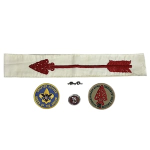 Puede incluir: Una colección de recuerdos de los Boy Scouts, que incluye una faja blanca con un diseño de flecha roja, dos parches circulares con texto, un pequeño alfiler y un alfiler rectangular. Los parches presentan las palabras "Chapter Adviser" y "Order of the Arrow".