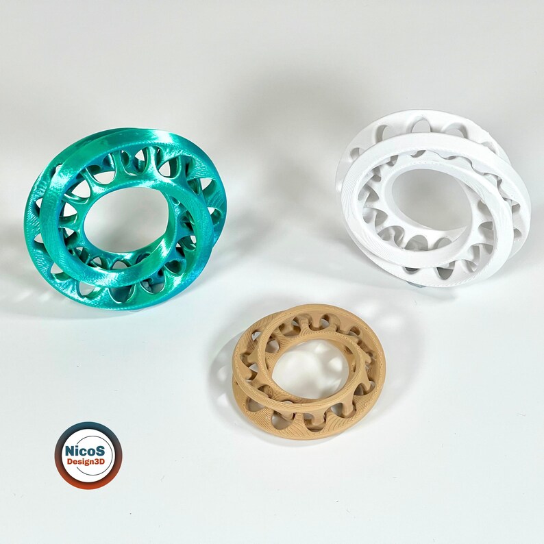 Das Foto zeigt zwei Möbius-Ring-Fidgets mit verschlungenen Schlaufen in Türkis und Weiß. Beispielansicht zum digitalen STL-Modell.