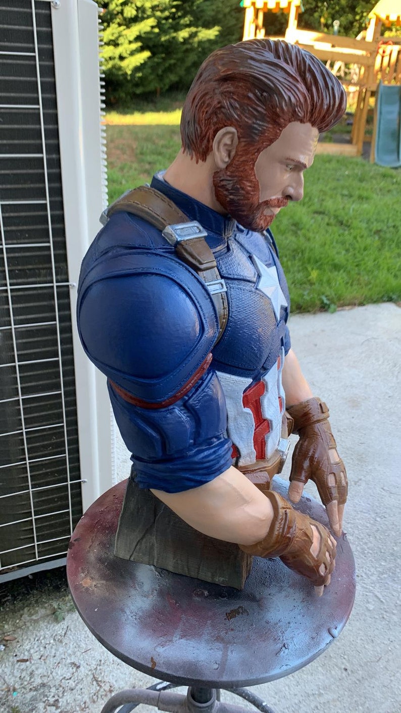 K&ouml;nnte beinhalten: Eine blaue und rote Captain America B&uuml;ste mit einem braunen Lederriemen und braunen Lederhandschuhen. Die B&uuml;ste ist aus bemaltem Kunststoff und eine Sammlerfigur.