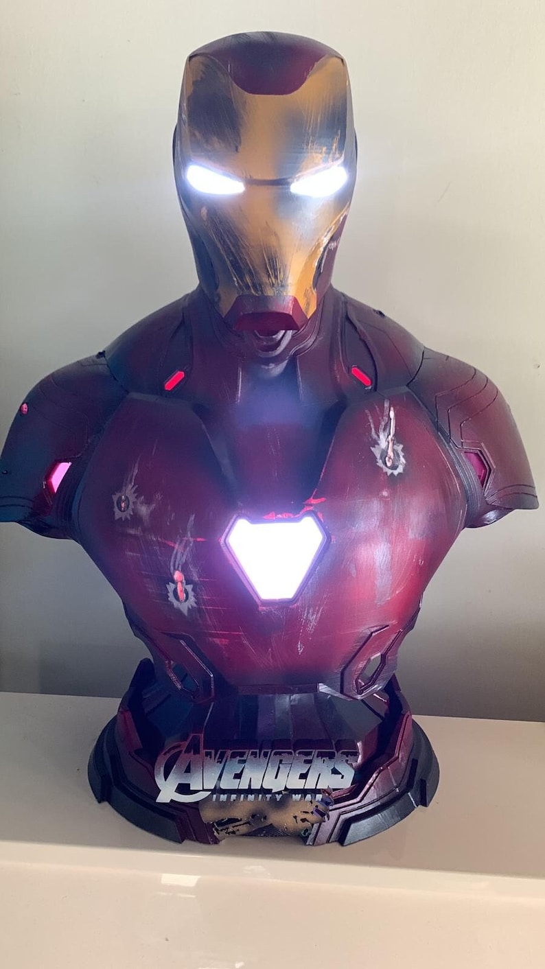 May include: A detailed bust of Iron Man, in red and gold with battle damage. The eyes and chest arc reactor glow brightly. The base displays the Avengers: Infinity War logo.