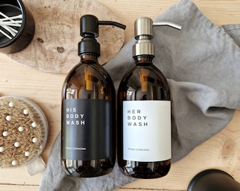 May include: Two amber glass bottles with black pump tops and white labels. The labels read "His Body Wash" and "Her Body Wash" with the text "Home Collection" below.