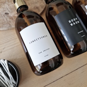 May include: Three amber glass bottles with black and white labels. The labels read "CONDITIONER THE SMITHS 500ML", "BODY WASH STEVEN 500ML", and "SHAMPOO STEVEN 500ML".