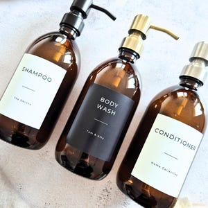 Peut inclure: Trois flacons en verre ambré avec pompes distributrices. Le premier porte une étiquette blanche SHAMPOO et The Smiths. Le deuxième une étiquette noire BODY WASH et Tom & Amy. Le troisième une étiquette blanche CONDITIONER et Home Collection.