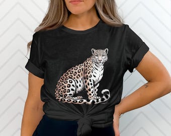 Puede incluir: Camiseta negra con una ilustración detallada de un leopardo. El leopardo tiene un pelaje manchado y está sentado con la cola enroscada. El diseño está centrado en la camiseta, ofreciendo un aspecto llamativo.