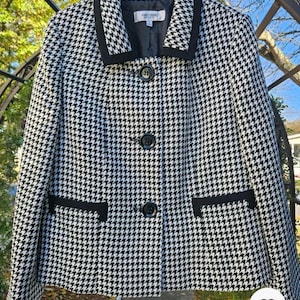 May include: A black and white houndstooth jacket with a notched collar and three black buttons. The jacket has black trim on the collar, pockets, and cuffs. The label reads "Jones Studio".