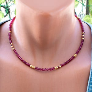 Puede incluir: Un delicado collar con pequeñas cuentas de color rojo oscuro intercaladas con detalles dorados. El collar se muestra sobre un maniquí, mostrando su diseño y color. Las cuentas parecen estar espaciadas uniformemente.