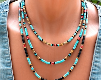 Puede incluir: Un collar de varias hebras con pequeñas cuentas cilíndricas en turquesa, negro, bronceado y rojo. Las cuentas están dispuestas en patrones repetitivos a través de tres capas distintas, creando un aspecto superpuesto con una paleta de colores consistente.