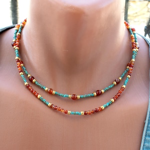 May include: Double-strand necklace with turquoise, orange, and gold beads. The necklace features small turquoise beads, with orange and gold accents. The necklace is displayed on a person.