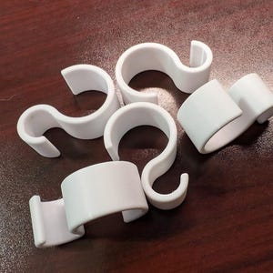 May include: Five white plastic hooks with a curved shape. The hooks are designed to hang items on a rod or bar.