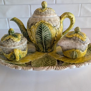 May include: A vintage ceramic tea set with a teapot, creamer, and sugar bowl. The set features a green and yellow leafy design with a white background.