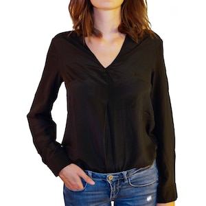 May include: A black long-sleeved blouse with a v-neckline and a relaxed fit. The blouse is tucked into a pair of blue jeans.