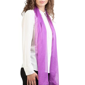 Pode incluir: Um lenço lavanda transparente sobre uma camisa branca. O lenço é de cor lisa e parece ser feito de um tecido leve. A pessoa está usando calças pretas.