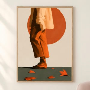May include: A framed wall art print featuring a person wearing a light beige jacket and rust-coloured trousers, standing on a dark grey surface with scattered orange autumn leaves. A large, solid orange circle is positioned behind the figure.