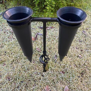May include: Black metal double flower vase holder with two black plastic cones. The holder is designed to be inserted into the ground.