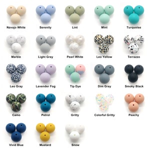 Könnte beinhalten: Eine Sammlung von Silikonperlen in verschiedenen Farben, darunter Navajo White, Serenity und Mint. Jede Gruppe von drei Perlen ist mit ihrem Farbnamen beschriftet. Weitere Farben sind Leo Yellow, Terrazzo und Smoky Black. Die Perlen sind wahrscheinlich für Bastelarbeiten oder die Schmuckherstellung.
