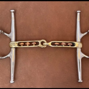May include: A silver horse bit with a copper roller and a gold-colored mouthpiece. The bit is marked "ASSAL FORGE" and "5".