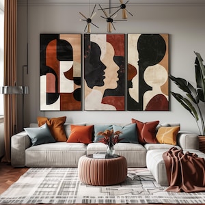 May include: Three abstract art prints with geometric shapes and silhouettes of faces in shades of brown, red, and white. The prints are hung on a wall above a white couch with pillows in shades of brown, blue, and green.